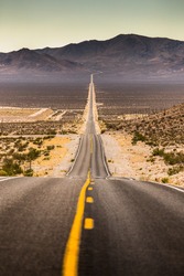 Classic vertical view of an endless straight road running through the barren scenery of famous Death Valley with extreme heat haze on a beautiful sunny day with blue sky in summer, California, USA