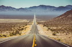 Classic vertical panorama view of an endless straight road running through the barren scenery of the American Southwest with extreme heat haze on a beautiful hot sunny day with blue sky in summer