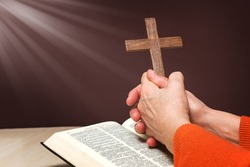 Closeup of wooden Christian cross and hand next on holy Bible