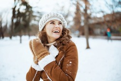 smiling elegant woman with mittens in a knitted hat and sheepskin coat outside in the city park in winter.
