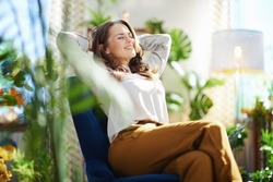 Green Home. relaxed stylish woman with long wavy hair at modern home in sunny day in green pants and grey blouse sitting in a blue armchair.
