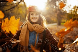 Hello autumn. Portrait of happy elegant female in red hat with scarf throwing autumn leafs in the city park.