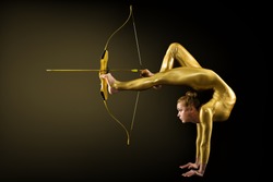 Archer Shooting by Legs with Gold Bow and Arrow. Flexible Gymnast aiming Target standing on Hand upside down. Goal Achievement Concept, Studio shot over Black background