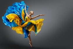 Beautiful Woman Ballet Dancer Jumping in Air in Colorful Fluttering Dress. Graceful Ballerina Dancing in Yellow Blue Gown over Gray Studio Background