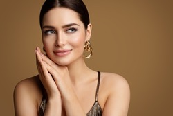 Woman Beauty with Smooth Skin Make up and Golden Jewelry. Beautiful Girl with Perfect Lips and Eye Makeup holding Hands under Chin. Elegant Model Portrait with Gold Earring smiling