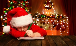 Christmas Child Write Letter to Santa Claus, Kid in Santa Hat Writing Wish List, unfocused lights background