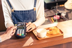Close-up of asian customer using his credit card with contactless nfs technology to pay a barista for his coffee purchase at a cafe bar.