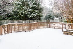 Snow on wood deck and fence with evergreens in background