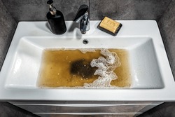 Clogged white sink in bathroom, sink with dirty water, brown soap. Plumbing problems.