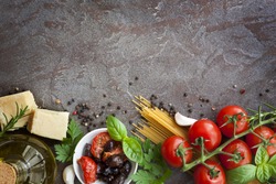 Italian food background, with vine tomatoes, basil, spaghetti, mushrooms, olives, parmesan, olive oil, garlic, peppercorns, rosemary, parsley and thyme.  Slate background.