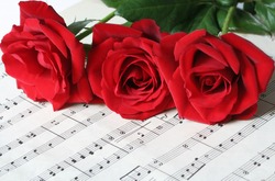 Three red roses, resting on old sheet music.