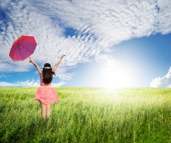 Beautiful woman holding red umbrella in green grass field and cloud sky