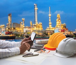 engineering working on computer tablet  against beautiful oil refinery background