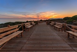 Weathered lumber path leading to calm sea during beautiful sunset in countryside in Cabopino, Artola dunes. Marbella, Spain
