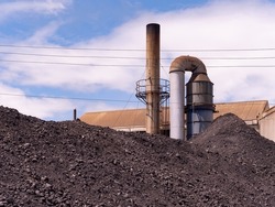 Heaps of coal used to produce steam with boilers at industrial plant. Smoke stack of boiler in the background.