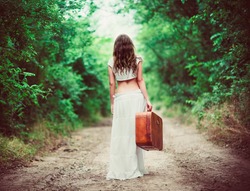 Young woman with suitcase in hand going away by a rural road
