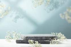 Flat granite pedestal and white flowers on blue background. Stone stand for natural design concept. Horizontal image, center composition, hard light, front view