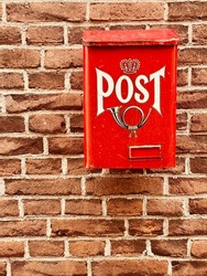 Traditional old bright red metal post box with word and picture of horn on front attached to the facade of the house, old brick wall of the home. Postal service posting mail letters and small packages