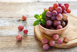 Bowl with pink grapes on a wooden stand.