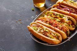 Hot dogs fully loaded with assorted toppings on a tray. Food background with copy space.