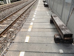 The old wooden bench which is made from the old sleeper tie on the concrete platform of the station in the city, front view for the copy space.