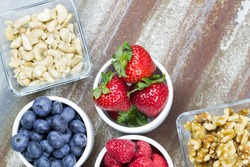 Healthy snack foods with small bowls of raspberries, blueberries, strawberries, cashews and walnuts