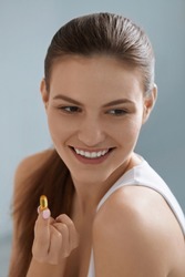Vitamin. Smiling woman with omega 3 pill, fish oil capsule in hand. Closeup portrait of beautiful girl taking vitamin D, E supplement. Diet nutrition concept