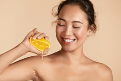 Beauty. Woman with radiant face skin squeezing orange in hand portrait. Beautiful smiling asian girl model with natural makeup, glowing facial skin and citrus fruit. Vitamin C cosmetics concept