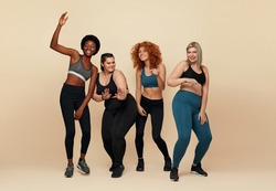 Diverse. Different Women Dancing Portrait. Diversity Figure And Size Models Full-Length Portrait. Group Of Multicultural Friends In Sportswear Posing On Beige Background. Body Positive As Lifestyle.