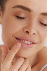 Lips Skin Care. Closeup Of Female Putting Lip Protector with Finger. Beautiful Woman With Satisfied Face, Applying Lip Balm with Her Hand. Portrait Of Female Model With Natural Makeup