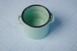 Photo of a soup pot on a graph paper. Toy pot is placed on millimeter grid page. Pot model for games. Cooking kitchenware for games. Paper with millimeter cells under the pot.
