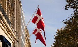 Two national flags of Denmark waving against blue sky in a sunny day on top of an old building.