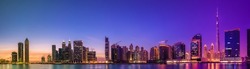 Cityscape of Dubai and panoramic view of Business bay with reflection of skyscrapers on water during purple sunrise, UAE