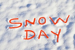 SNOW DAY written in bright red capital letters in fresh snowfall signifies No School and school closure due to dangerous weather conditions.
