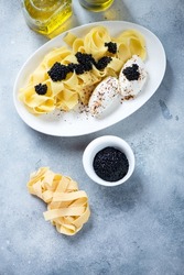 Pappardelle pasta with black caviar and cream-cheese on a white plate, vertical shot on a light-blue stone background, high angle view