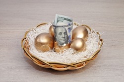 Golden eggs in nest with dollars on wooden background.  