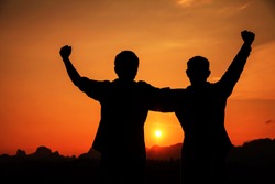 Silhouette of two man with success in sunset mountains.