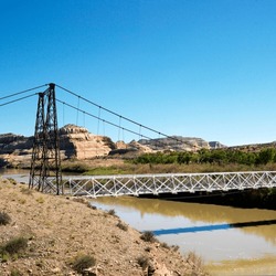 Suspension bridge over river with rock cliffs in Utah.