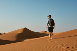 Young tourist in desert. Man with backpack walking on sand dune. Desert Wahiba Sands in Oman.