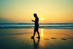 Silhouette of young man with mobile phone on the beach at sunset 