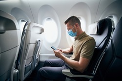 Man wearing face mask and using phone inside airplane during flight. Themes new normal, coronavirus and personal protection. 