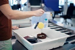 Airport security check before flight. Passenger holding plastic bag with liquids above container personal items. 