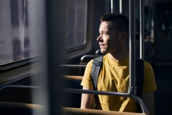 Pensive lonely man looking out of window of train. Solo traveler in public transportation on sunny day.