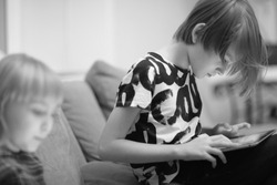 A boy and a girl are sitting on the sofa in the room and playing a computer game on a tablet