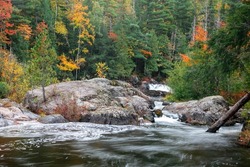 Large rocks in running water of Dead river surrounded with fall foliage in Michigan upper peninsula.