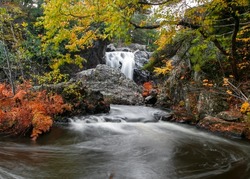 Large rock in running water of Dead river surrounded with fall foliage in Michigan upper peninsula.