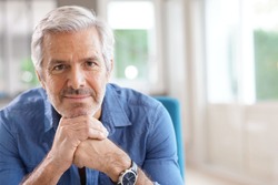Portrait of 60-year-old man with grey hair and blue shirt looking at camera