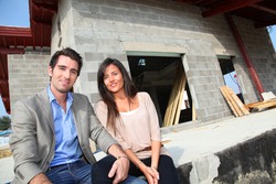 Happy couple sitting in front of house under construction