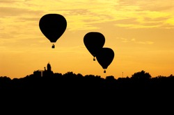 Three hot air balloons are silhouetted at sunset as the float above an Iowa landscape.