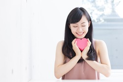 Cute young woman holding pink heart symbol